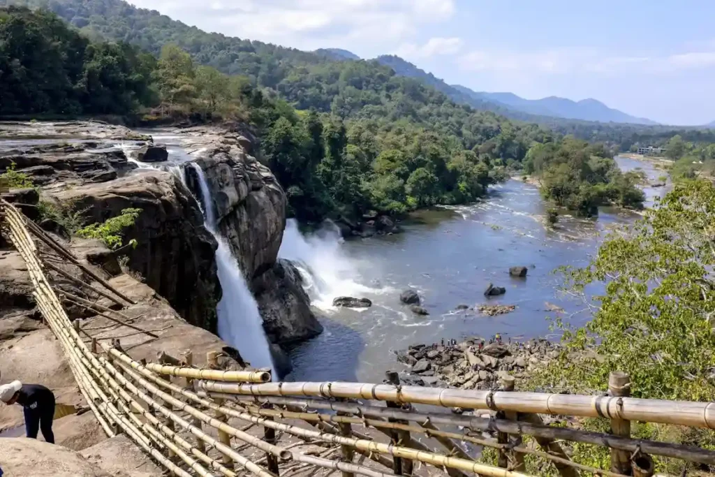 Athirappilly waterfall in Kerala flowing into a river surrounded by lush green forest during monsoon.