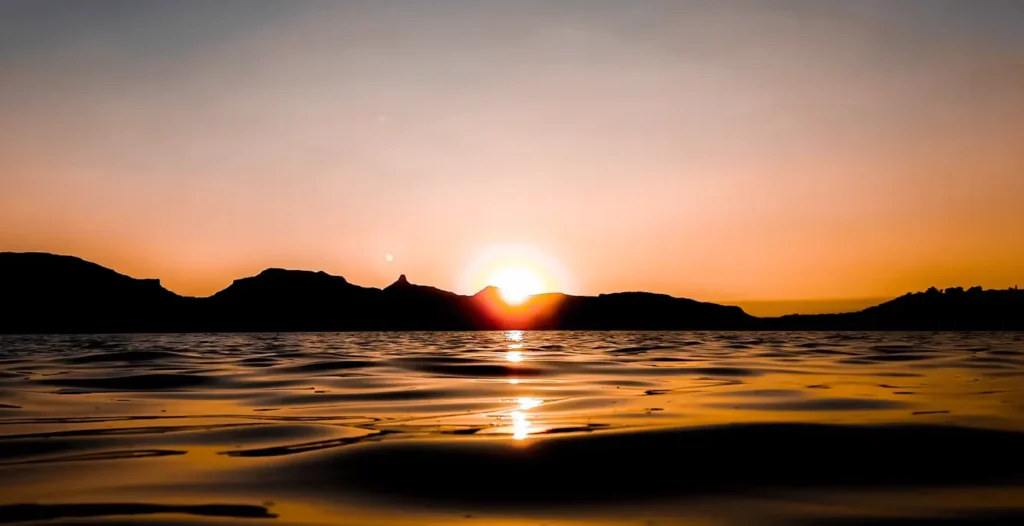 Sunset view over Bhandardara lake with golden sky reflections and mountain silhouettes in Maharashtra.